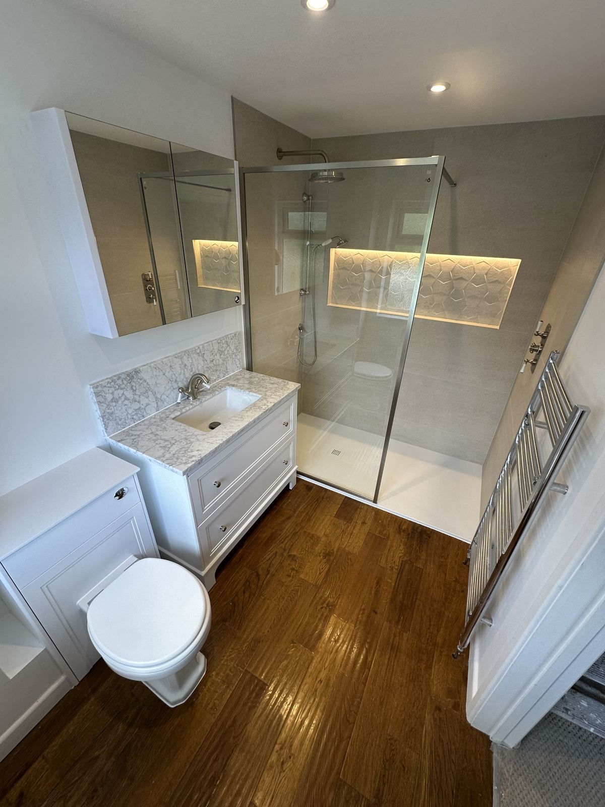 Walk-in shower with a back-lit textured niche and a white shaker vanity