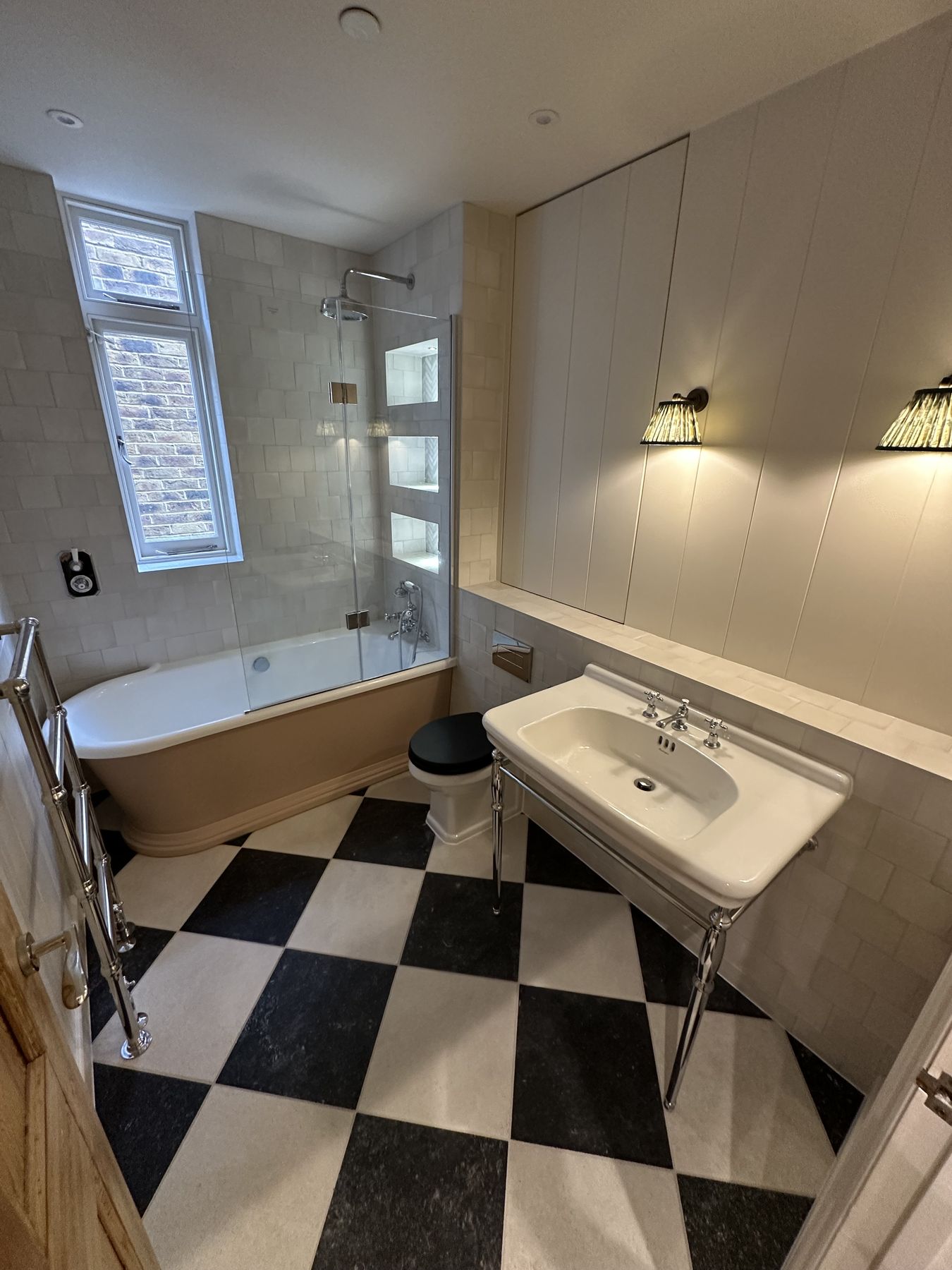 Period family bathroom with a black and white chequerboard floor, washstand basin and lit glass shelving