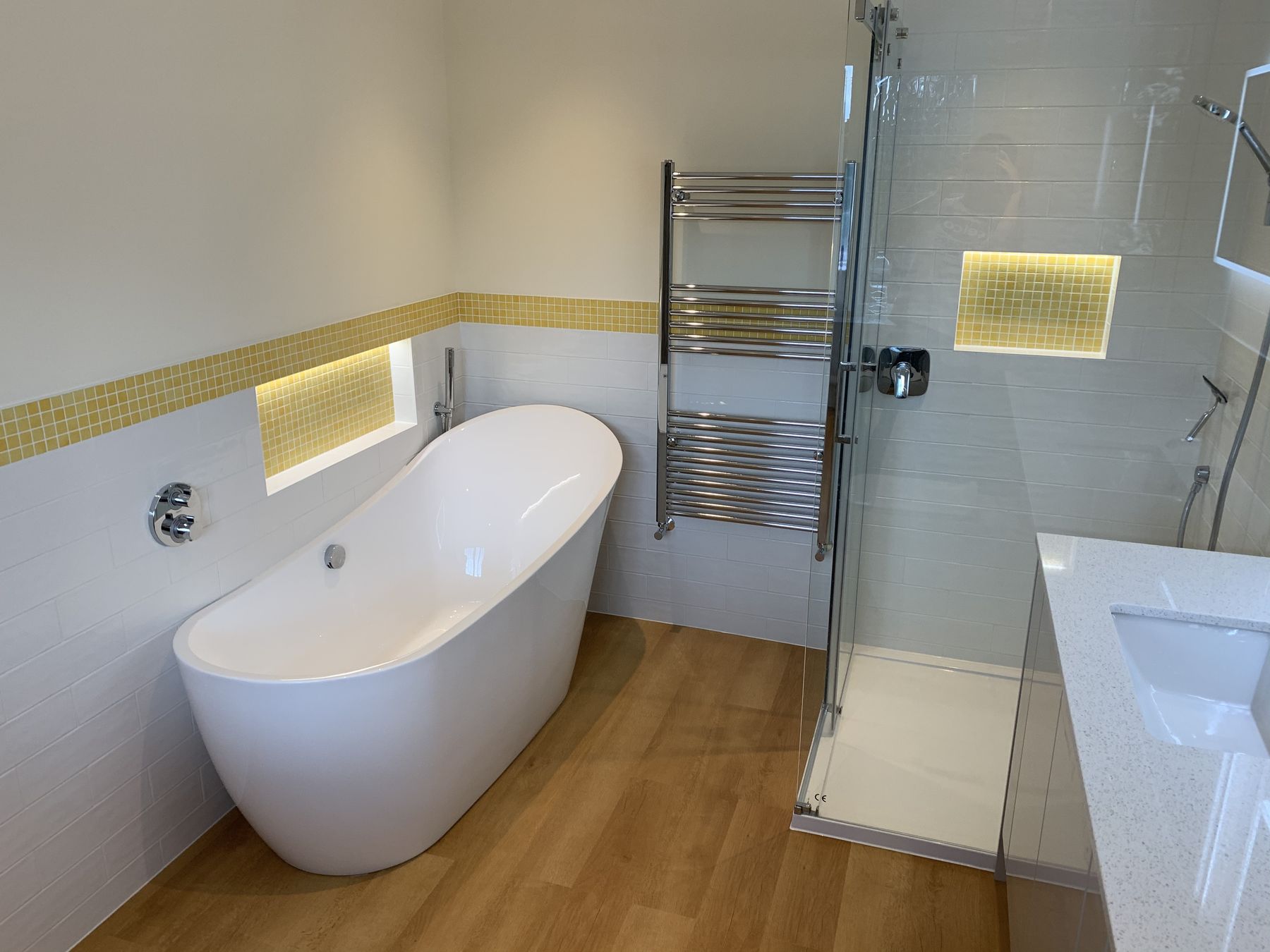 Finished bathroom with a freestanding slipper bath and a lit gold mosaic niche
