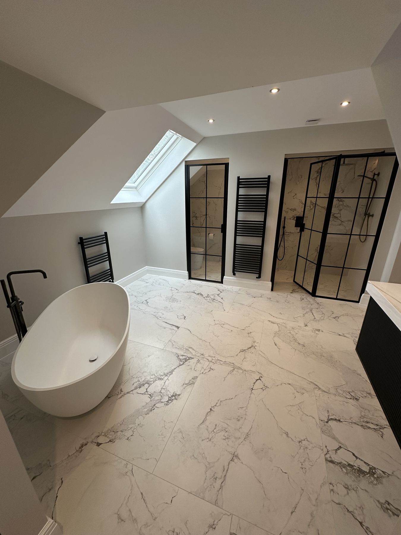 Loft master bathroom with marble-effect porcelain, a freestanding bath and black-framed screens