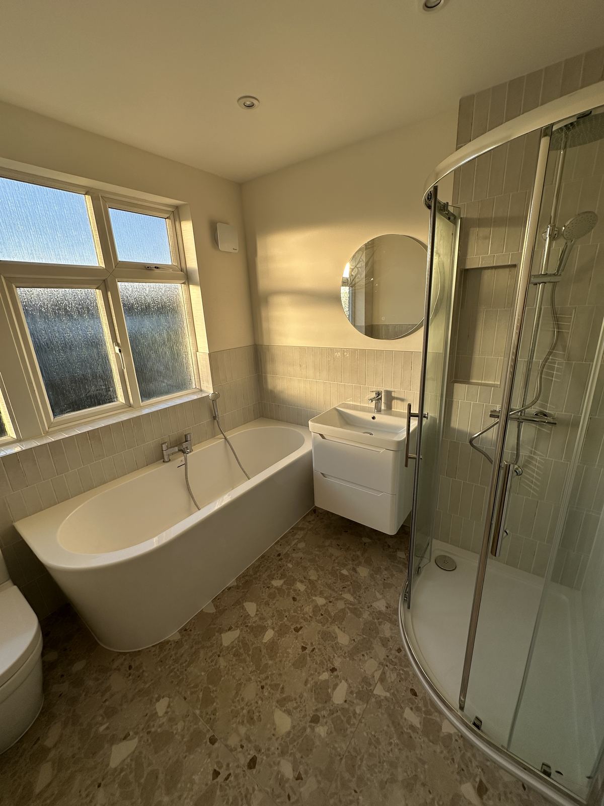 Sunlit family bathroom with a terrazzo floor and freestanding-style bath